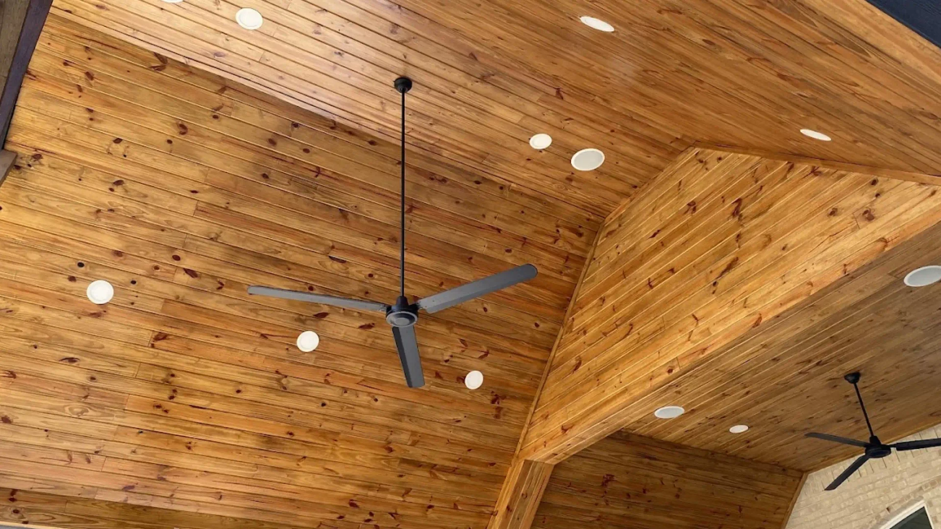 wooden light brown ceiling with some lights and a black fan